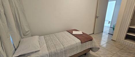 A small, neatly made bed with a patterned bedspread and a folded white towel.
