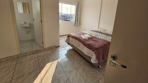 A hotel room with a bed, a bathroom with a sink, and a view of the city through the window.