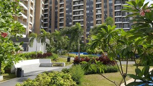 A modern apartment building with multiple balconies, surrounded by well-maintained greenery and a paved walkway.