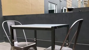 A metal table and two chairs on a tiled patio with a building in the background.