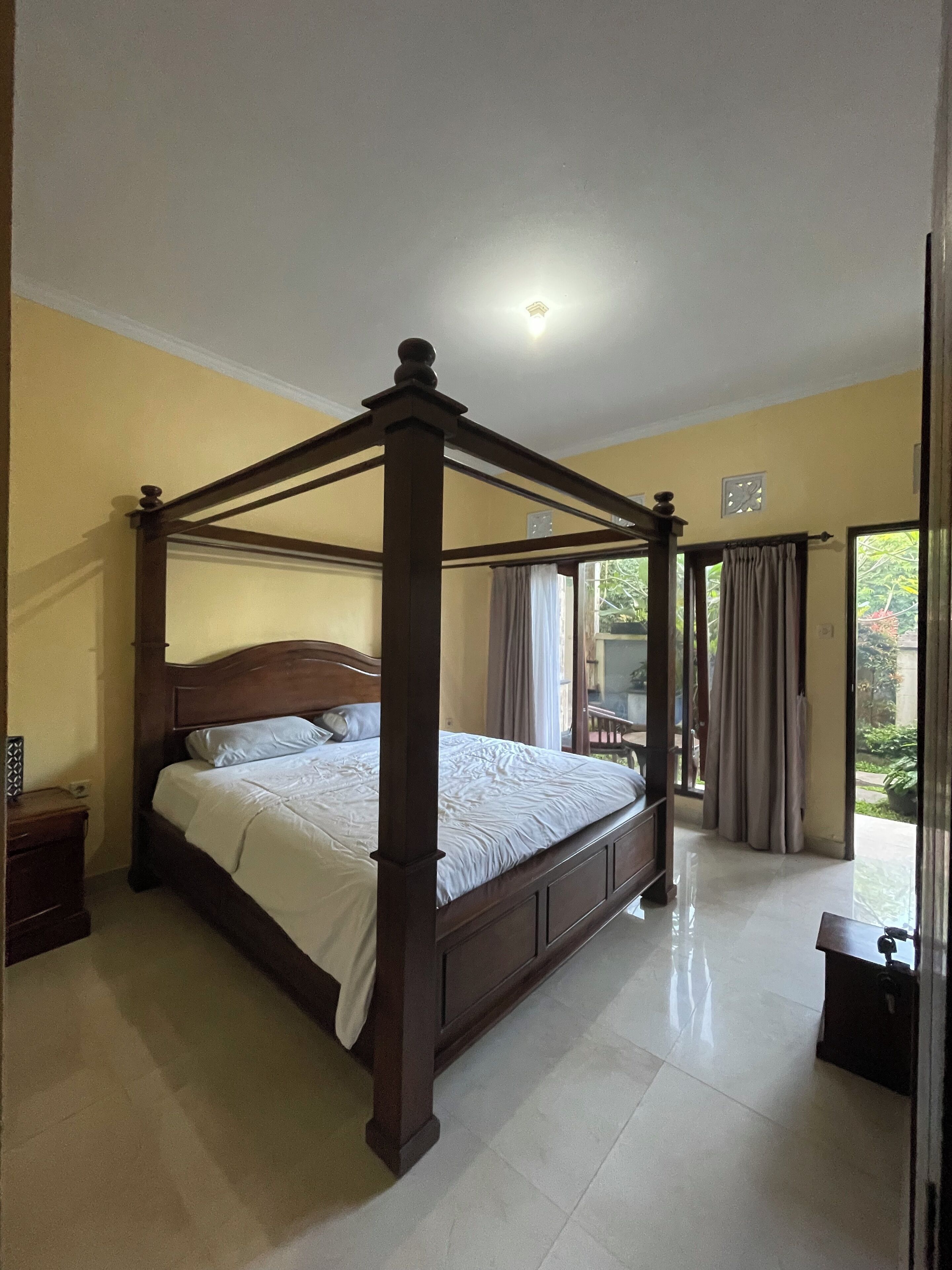Un lit à baldaquin dans une chambre dont le sol est carrelé et qui offre une vue sur l’extérieur.