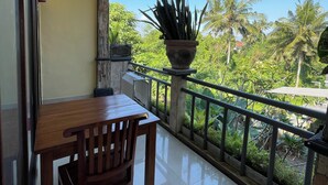 A balcony with a wooden table and chairs, a potted plant, and a view of palm trees and greenery. - Casa de cavin (Ubud)