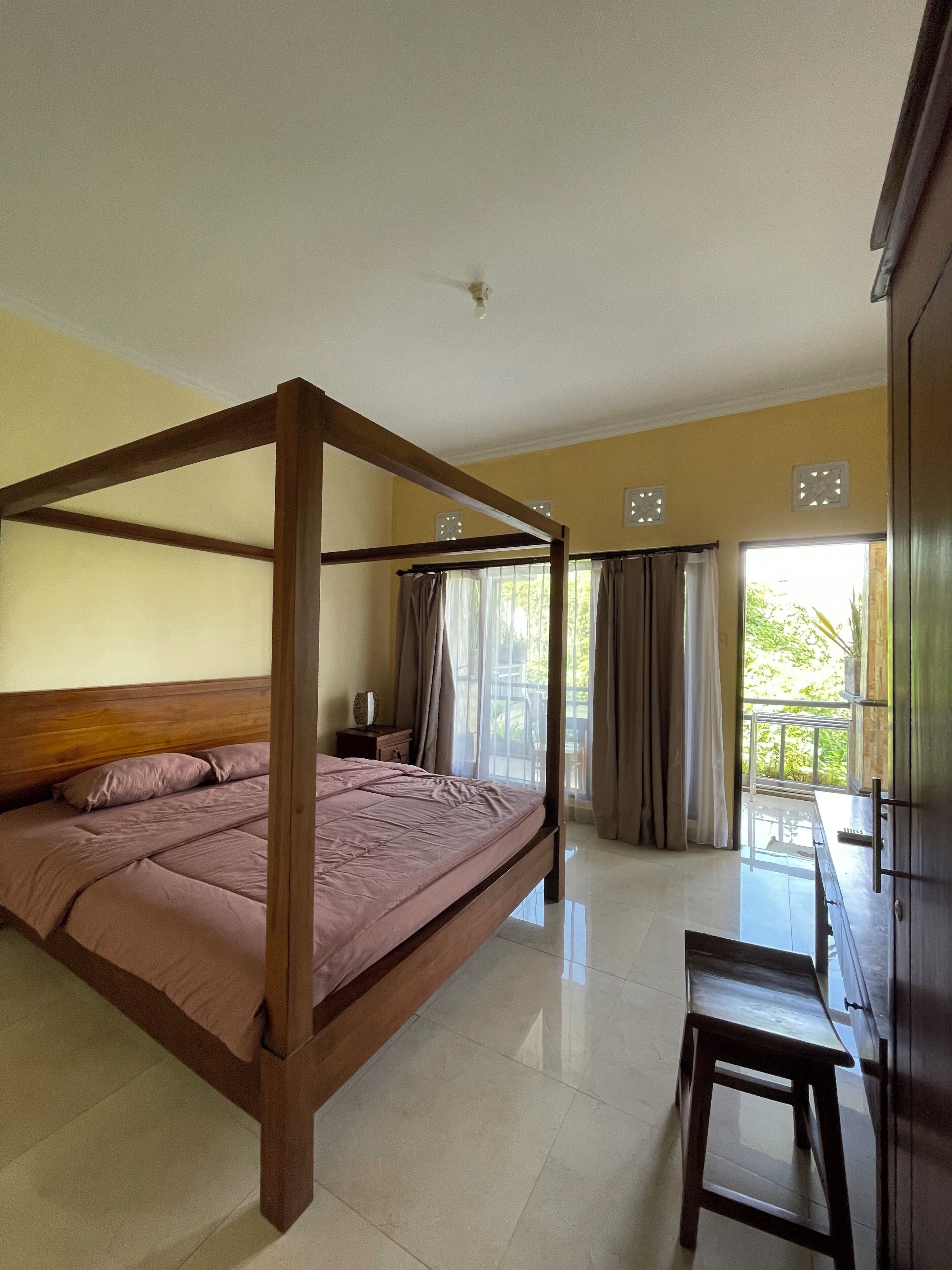 Un dormitorio con una cama con dosel, una mesita de noche, una silla y vistas al exterior a través de una ventana.
