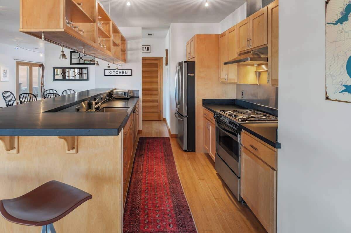 A modern kitchen with wooden cabinets, a black countertop, and a red rug.