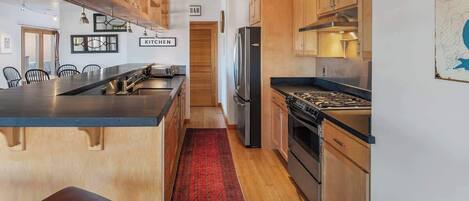 A modern kitchen with wooden cabinets, a black countertop, and a red rug.