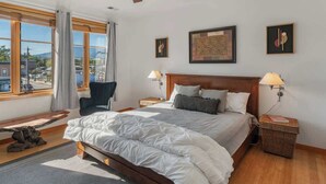 Hotellihuone, jossa on suuri sänky, kaksi yöpöytää valaisimineen, tuoli, näkymä ulos ja taideteoksia seinillä.