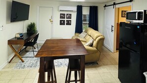 A compact living space with a dining table, a sofa, a TV, and a refrigerator. - Fantastic apartment with AC in charming downtown Leesburg (Leesburg)