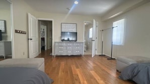 Un dormitorio con dos camas, un aparador, un televisor y un pasillo que conduce a otra habitación.