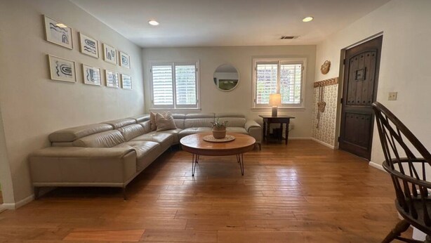 Una sala de estar con un sofá seccional color beige, una mesa de centro redonda y piso de madera.