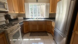 Una cocina con armarios de madera, un refrigerador de acero inoxidable, una estufa y una ventana con contraventanas.