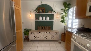 Una cocina con armarios de madera, un refrigerador de acero inoxidable, una estufa blanca y un estante verde con la palabra 'HOME'.