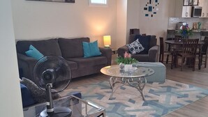 Un salon avec un canapé, une table basse et un ventilateur. Il y a également un coin repas avec une table et des chaises.