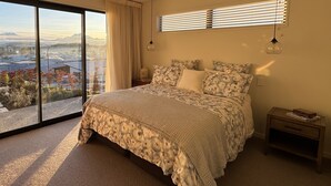 Une chambre avec un grand lit, une table de chevet, une fenêtre avec des stores et une vue sur le paysage urbain.