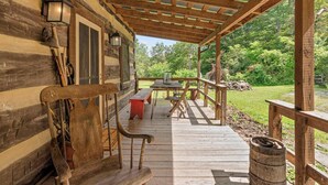 A wooden cabin with a covered porch, a red bench, and a table with chairs.