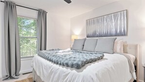 Een slaapkamer met een bed, een raam met gordijnen, een wandlamp en een schilderij.