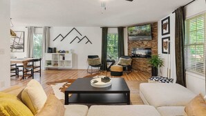 Een ruime woonkamer met een open haard, een plafondventilator en een eethoek met een houten tafel en stoelen.