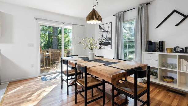 Een eetgedeelte met een houten tafel, zwarte stoelen, een hanglamp en een boekenkast vol boeken en decoratieve objecten.