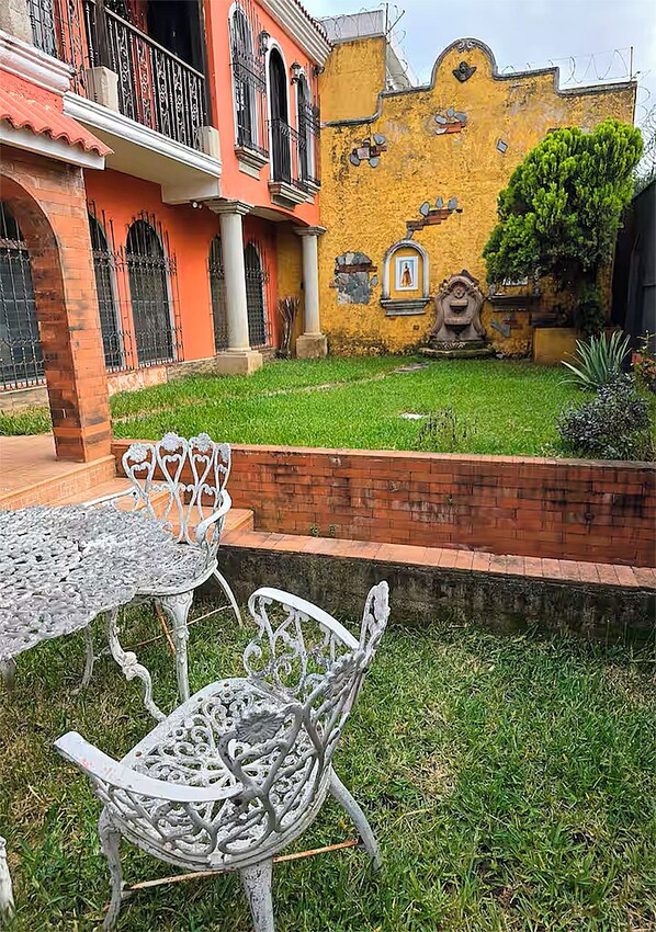 A courtyard with a metal table and chairs, a brick wall, and a yellow building with balconies and decorative elements.