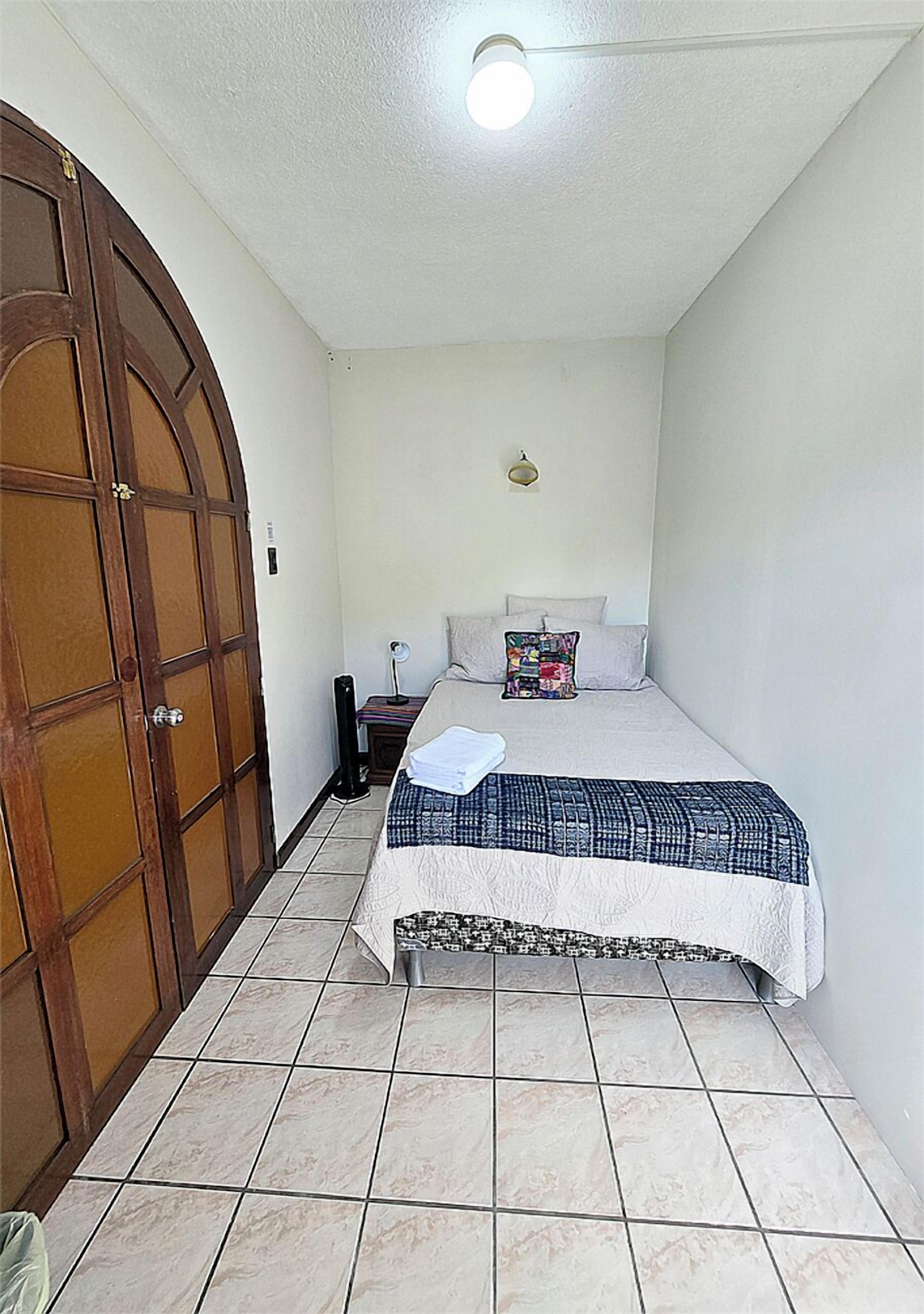 Un dormitorio con cama, mesita de noche, lámpara, armario y luz de techo.