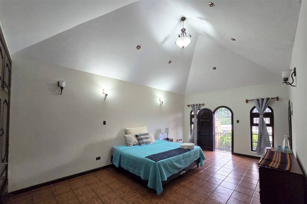 Une chambre à coucher avec un lit, une table de chevet, une lampe et une fenêtre avec des rideaux.