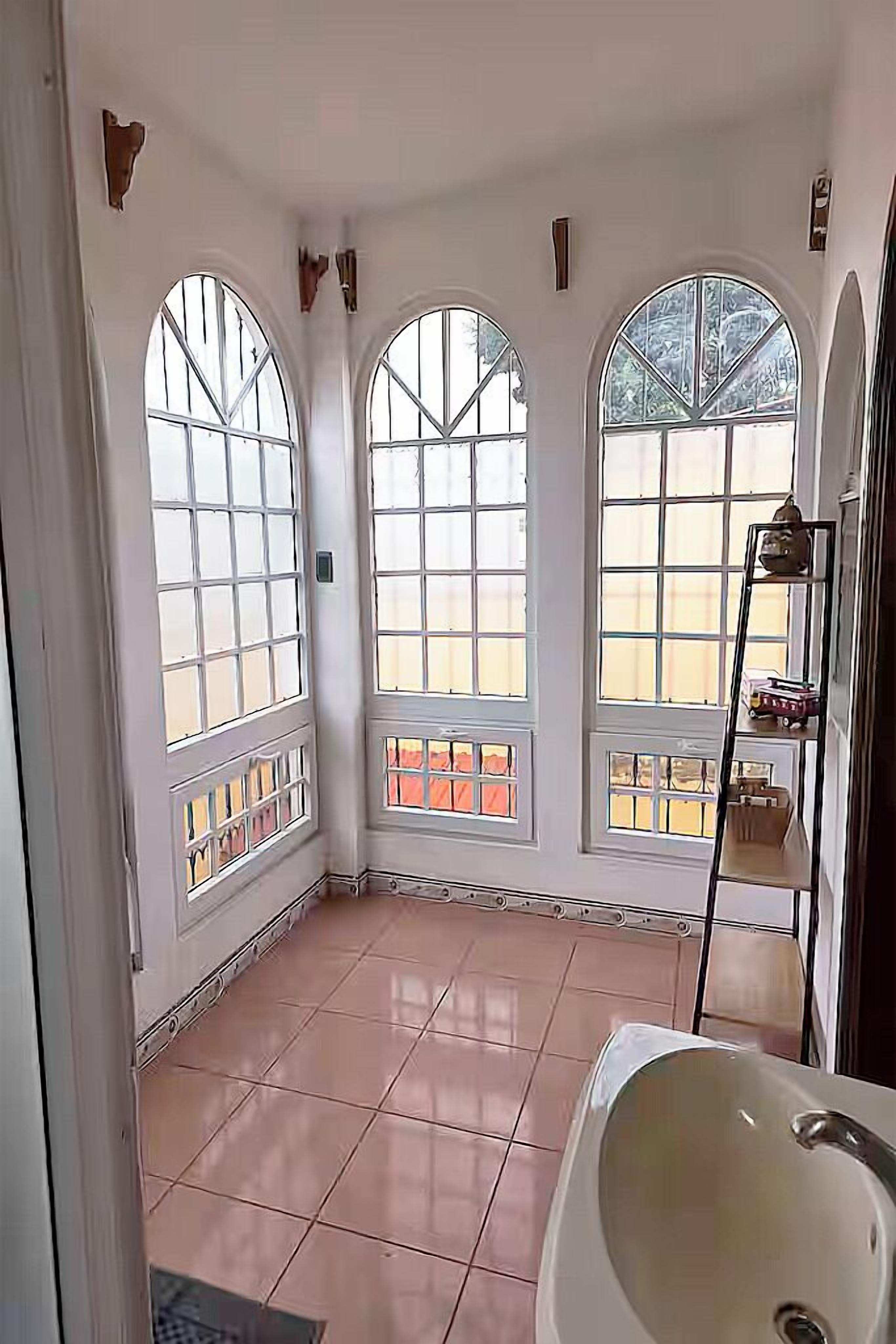 A bathroom with a large window, a bathtub, and a shelf with toiletries.