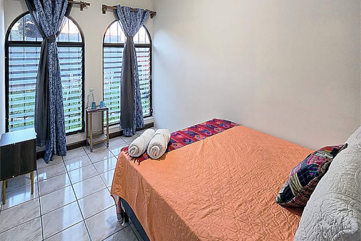 Une chambre à coucher avec un lit, des rideaux, une fenêtre et un sol carrelé.