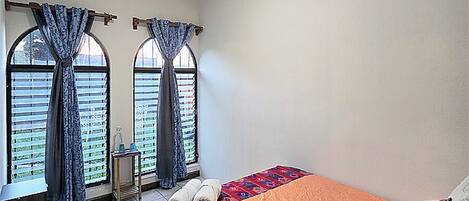 Un dormitorio con cama, cortinas, una ventana y suelo de baldosas.