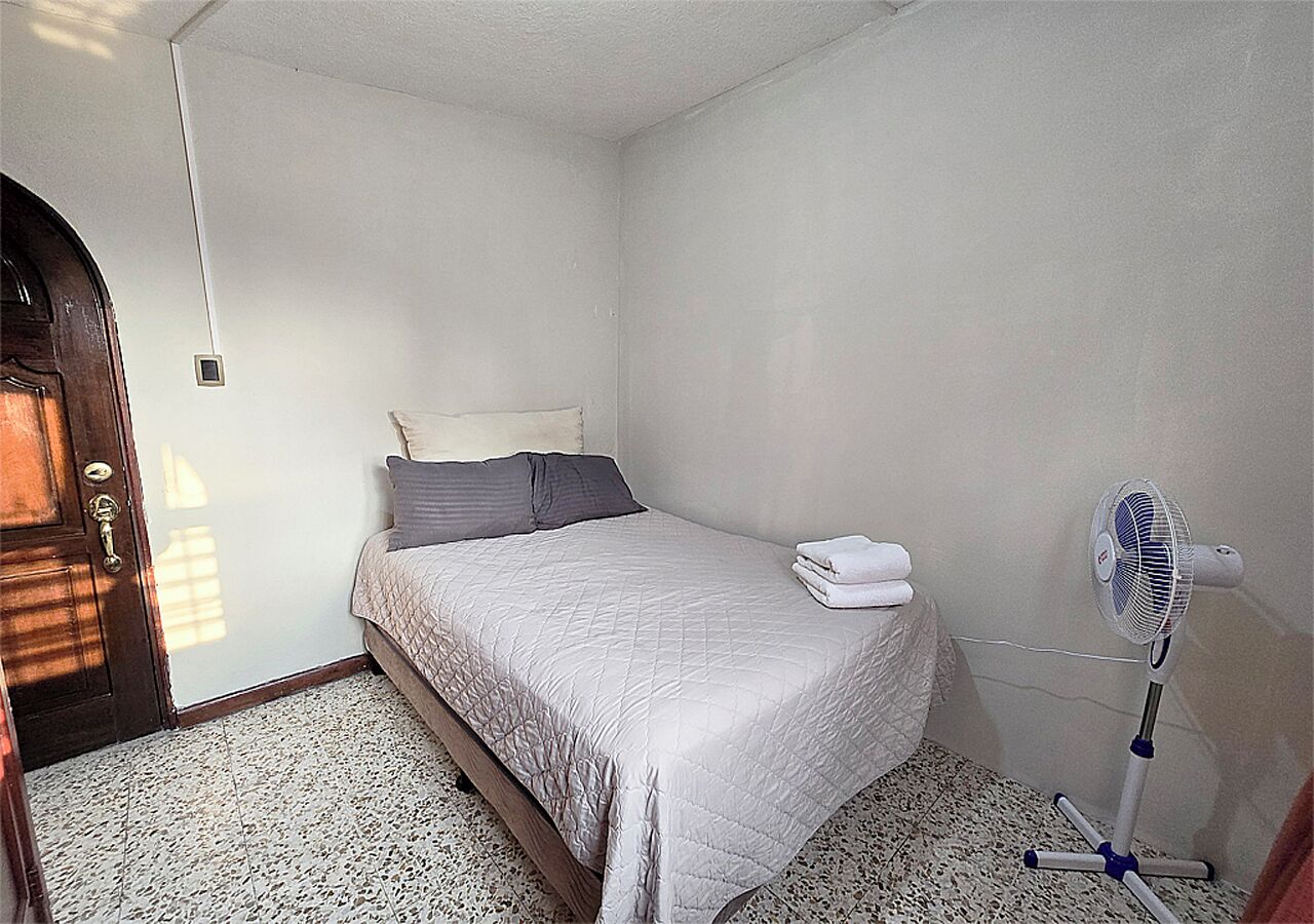A bedroom with a bed, pillows, a fan, and a door.