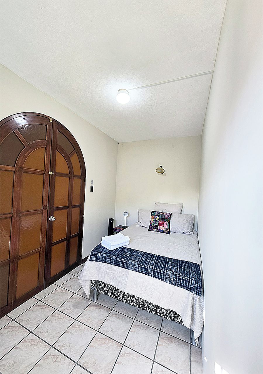 Un dormitorio con una cama, una puerta de madera, un accesorio de iluminación y suelo de baldosas.