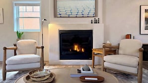 Una sala de estar con chimenea, dos sillones, una mesa de centro y un cuadro sobre la chimenea.