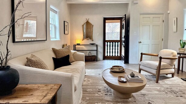 Una sala de estar con sofá, mesa de centro y sillón, un espejo y una puerta que da al exterior.