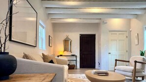 Una sala de estar con un sofá, una mesa de centro y una silla, una mesa de madera, un espejo y una puerta al fondo.