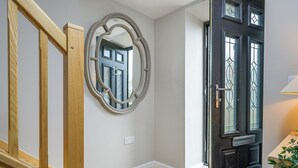 A hallway with a wooden staircase, a round mirror, a black door with glass panels, and a white wall.