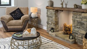 A living room with a stone fireplace, a television mounted on the wall, a cushioned armchair, and a coffee table with a tray of items.