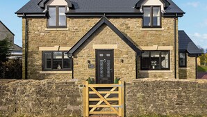 A stone house with a black door, two windows on the upper floor, and a small front gate.