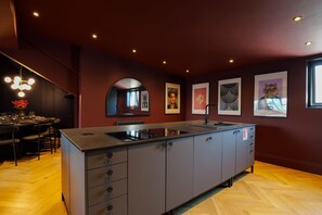 A modern kitchen with a central island, dark walls, and artwork.
