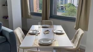 A dining area with a white table set for four, beige chairs with gold legs, and a view of buildings and trees through large windows with beige curtains. - Modern & central in the cityI 8 guests I kitchen I washing machine I balcony (Stuttgart)