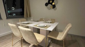 Ein Essbereich mit einem weißen Tisch, vier Stühlen mit goldenen Beinen und einer dekorativen Wandverkleidung.
