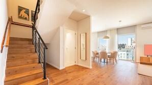 A spacious living area with a wooden staircase, a dining table with chairs, and a large window offering a city view. - GuestReady - Republic Apartments 8D (Lisbon)