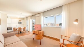 A modern living room with a sofa, chairs, a coffee table, and a TV. There is a kitchen in the background with a dining table and chairs. - GuestReady - Republic Apartments 8D (Lisbon)