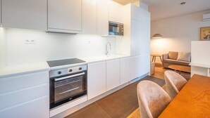 Een moderne keuken met witte kasten, een ingebouwde oven en een magnetron. Er is een eethoek met een houten tafel en stoelen.