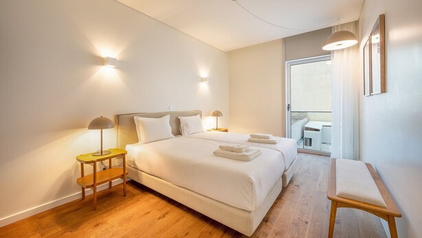 Een hotelkamer met een groot bed, twee nachtkastjes, een bankje en een balkon met een tafel en stoelen.