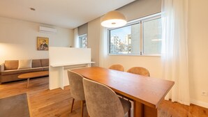 Een moderne woonkamer met een houten eettafel, comfortabele stoelen, een bank en een groot raam met gordijnen.