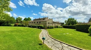 A stone building with a paved pathway leading to it, surrounded by well-maintained grass and hedges. - Historic Apartment 2 Bedroom 2 Bathroom near Cortona Tuscany with pool & grounds (Cortona)