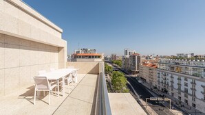 A terrace with a table and chairs, overlooking a cityscape with buildings and a clear sky. - GuestReady - Republic Apartments 8E (Lisbon)