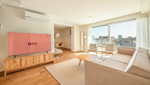 A modern living room with a flat-screen TV, a sofa set, a dining area, and large windows offering a city view. - GuestReady - Republic Apartments 8E (Lisbon)