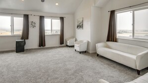 Ein geräumiges Wohnzimmer mit einem großen Fenster, einem weißen Sofa, einem kleinen weißen Sessel und einer schwarzen Mülleimer.