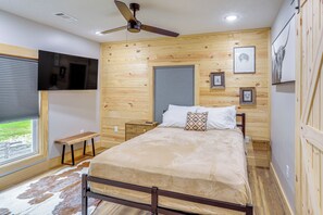 A bedroom with a bed, a ceiling fan, wooden walls, a window, and a mounted TV. - Relax on the River: Modern Mountain View Escape! (Mountain View)