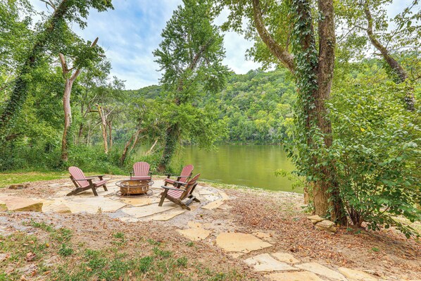 An outdoor seating area with Adirondack chairs and a fire pit, surrounded by a natural landscape and a body of water. - Relax on the River: Modern Mountain View Escape! (Mountain View)