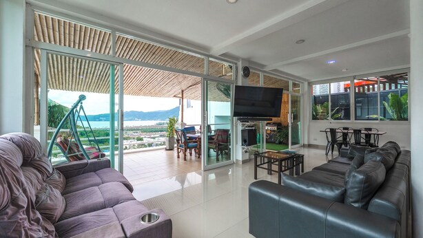 A modern living room with a large TV, comfortable seating, and a view of a cityscape through large glass doors. - 4BR PoolVilla and SeaView V199 (Patong)